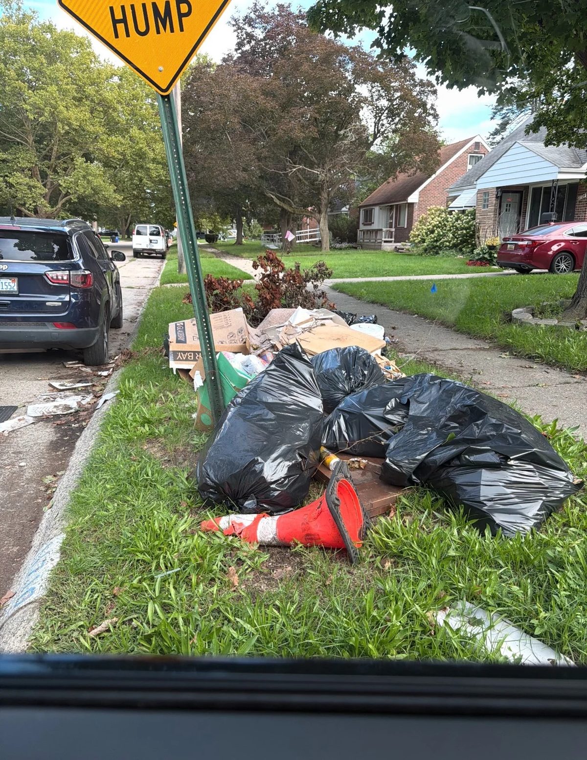 Trash bags, cardboard, and debris piled beside a neighborhood sidewalk before pickup